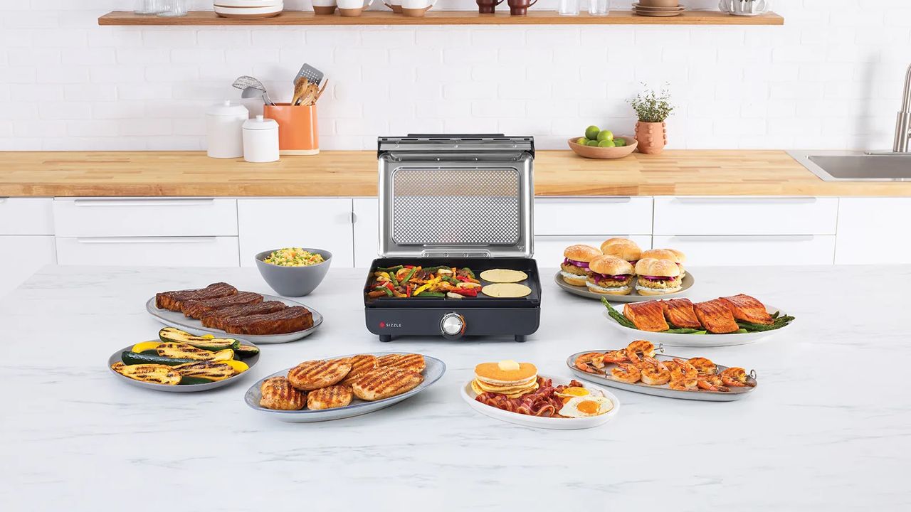 The Ninja Sizzle indoor grill surrounded by food cooked on the flat plate