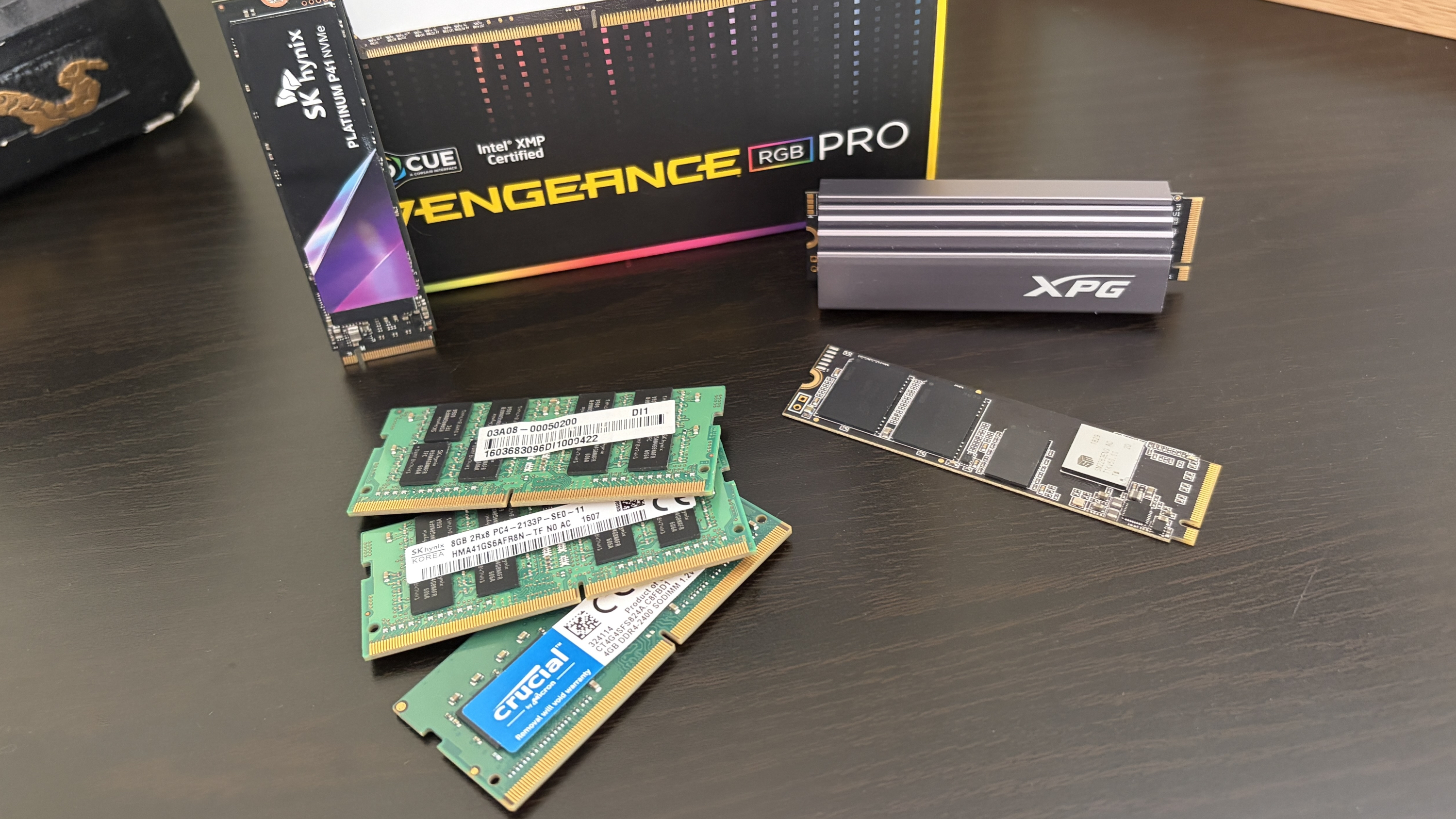 A collection of computer memory components, including green RAM sticks, a silver heatsink labeled "XPG," and a black M.2 SSD.