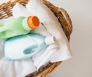 A laundry basket with fodled sheets and laundry detergent bottles