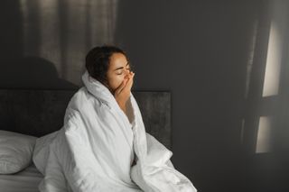 A woman yawning with a duvet wrapped around her shoulders
