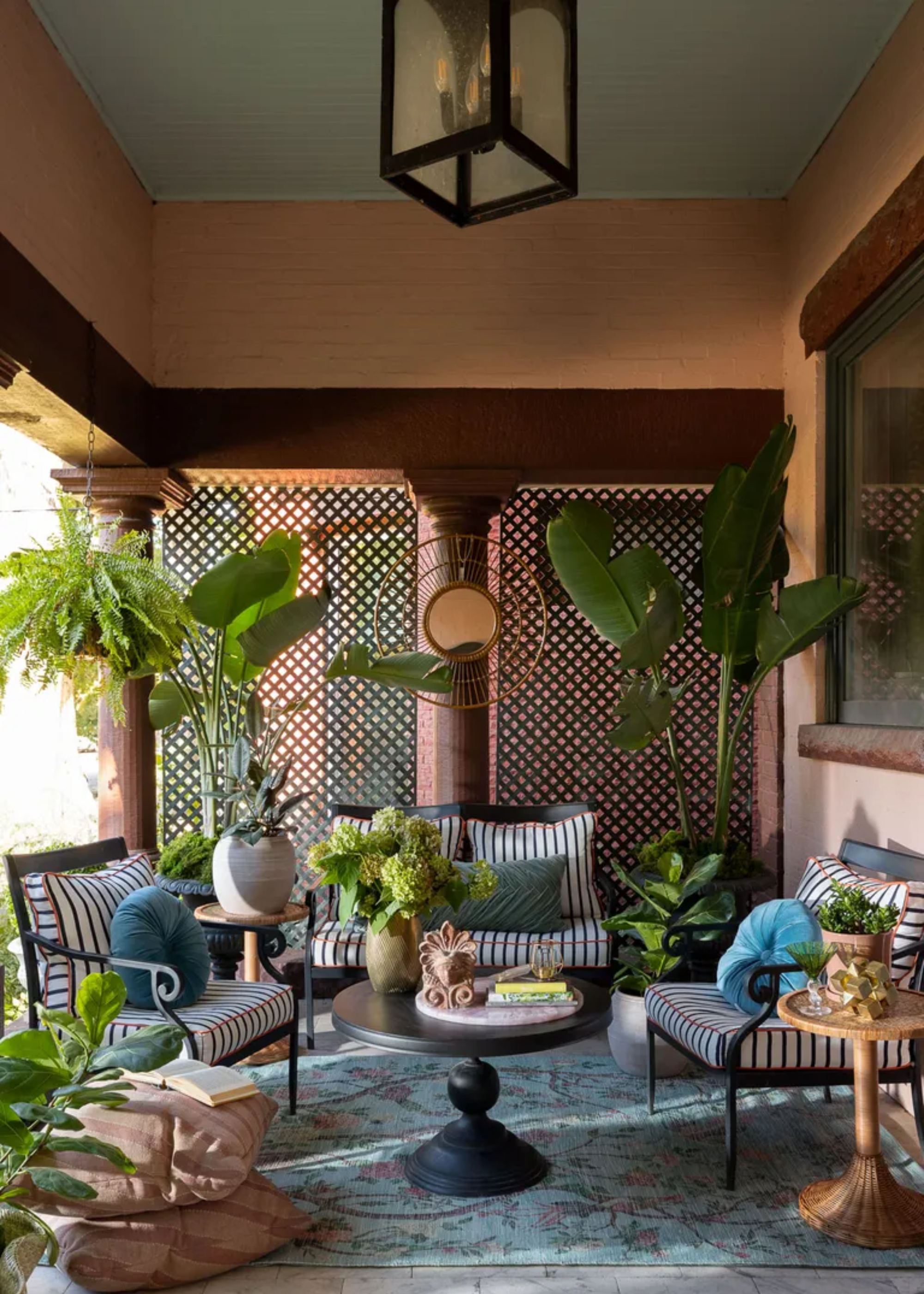 A beautifully decorated balcony with potted plants, an outdoor rug, a set of side tables, and seating with striped cushions