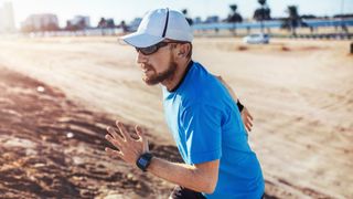 Mid adult man wearing baseball cap running up sand dune