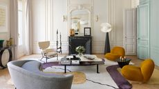 french apartment with ornate wall molding, two mustard yellow armchairs, a gray sofa, and patterned rug in front of a black marble fireplace