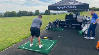 A golfer lines up to hit a shot in front of a TaylorMade tent