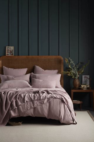 Bed with pale rose bed linen in dark navy room