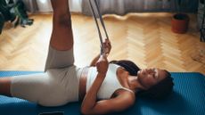 Woman lays on yoga mat to exercise using a resistance band