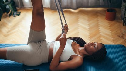 Woman lays on yoga mat to exercise using a resistance band