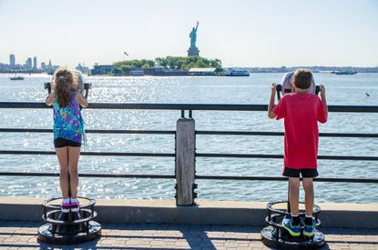 Kids looking at Statue of Liberty through paying binoculars from the Liberty State Park in Jersey city during summer day