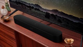 A black Sonos Beam Gen 2 in front of a TV on top of a wooden rack