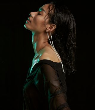 Woman wearing two long dangling pearl earrings against a black background