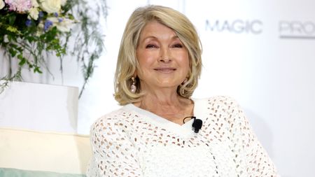 Martha Stewart with a blonde bob wearing a white shirt, with a vase of white flowers and a white backdrop behind it