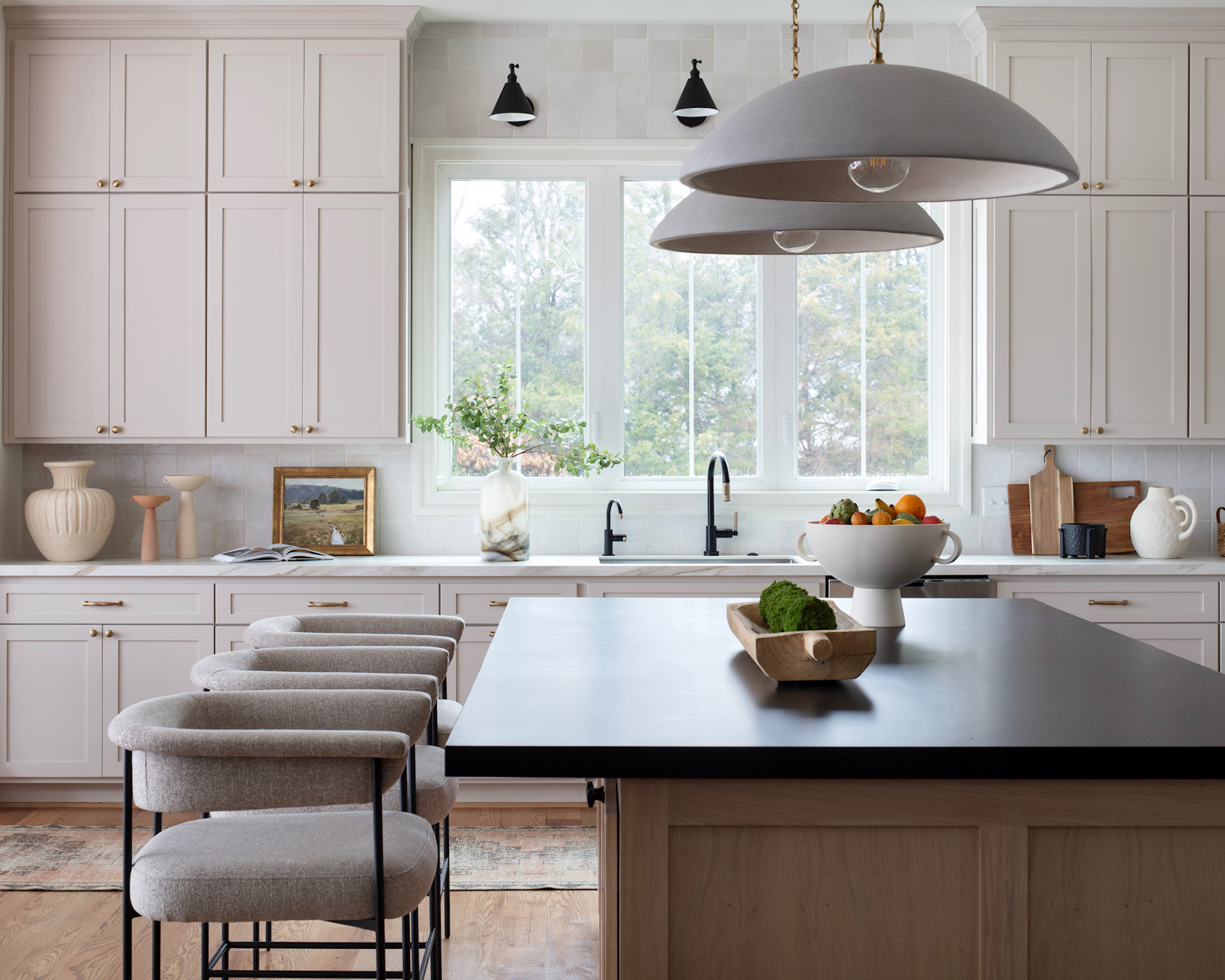 Kitchen with beige cabinets, wood island with beige upholstered bar stools and pendant lights over and black bar stools