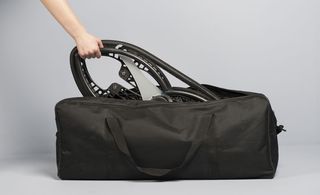 A hand holding the handle of a black luggage bag, photographed against a grey background