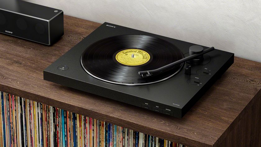 A black Sony PS-LX310BT turntable positioned on a wooden sideboard next to a wireless speaker. A collection of records is visible stored underneath.