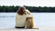 A woman sits on a doc with her arm around her dog.