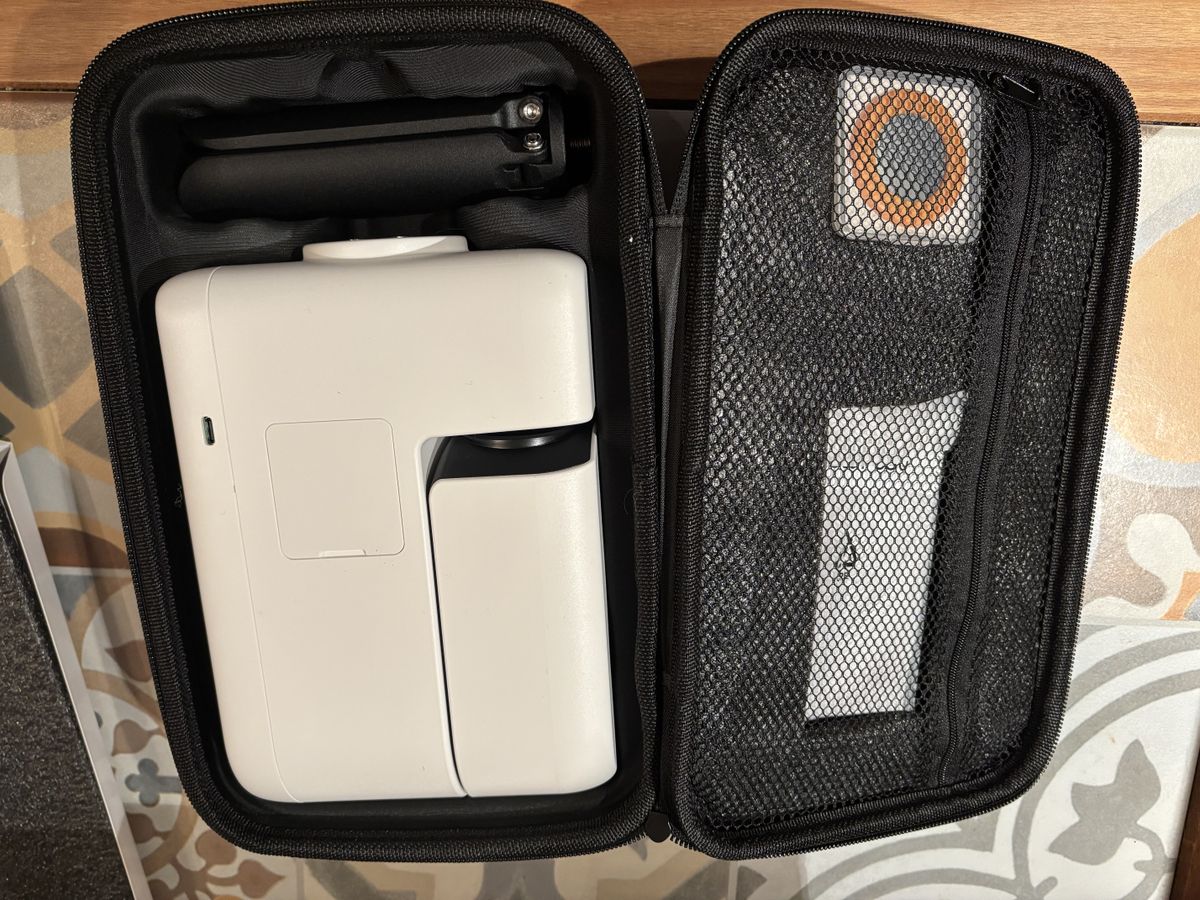 A carry bag is opened up and inside is a black tripod (folded) , a white smart telescope (also folded) on the left while on the right, some accessories are in a zipped-up section.