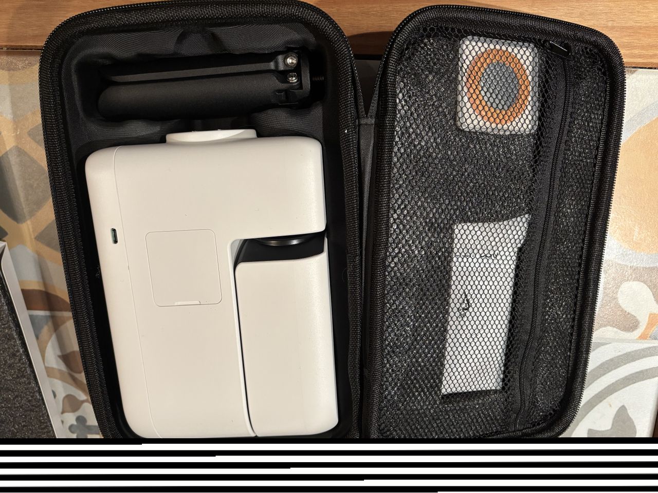 A carry bag is opened up and inside is a black tripod (folded) , a white smart telescope (also folded) on the left while on the right, some accessories are in a zipped-up section.