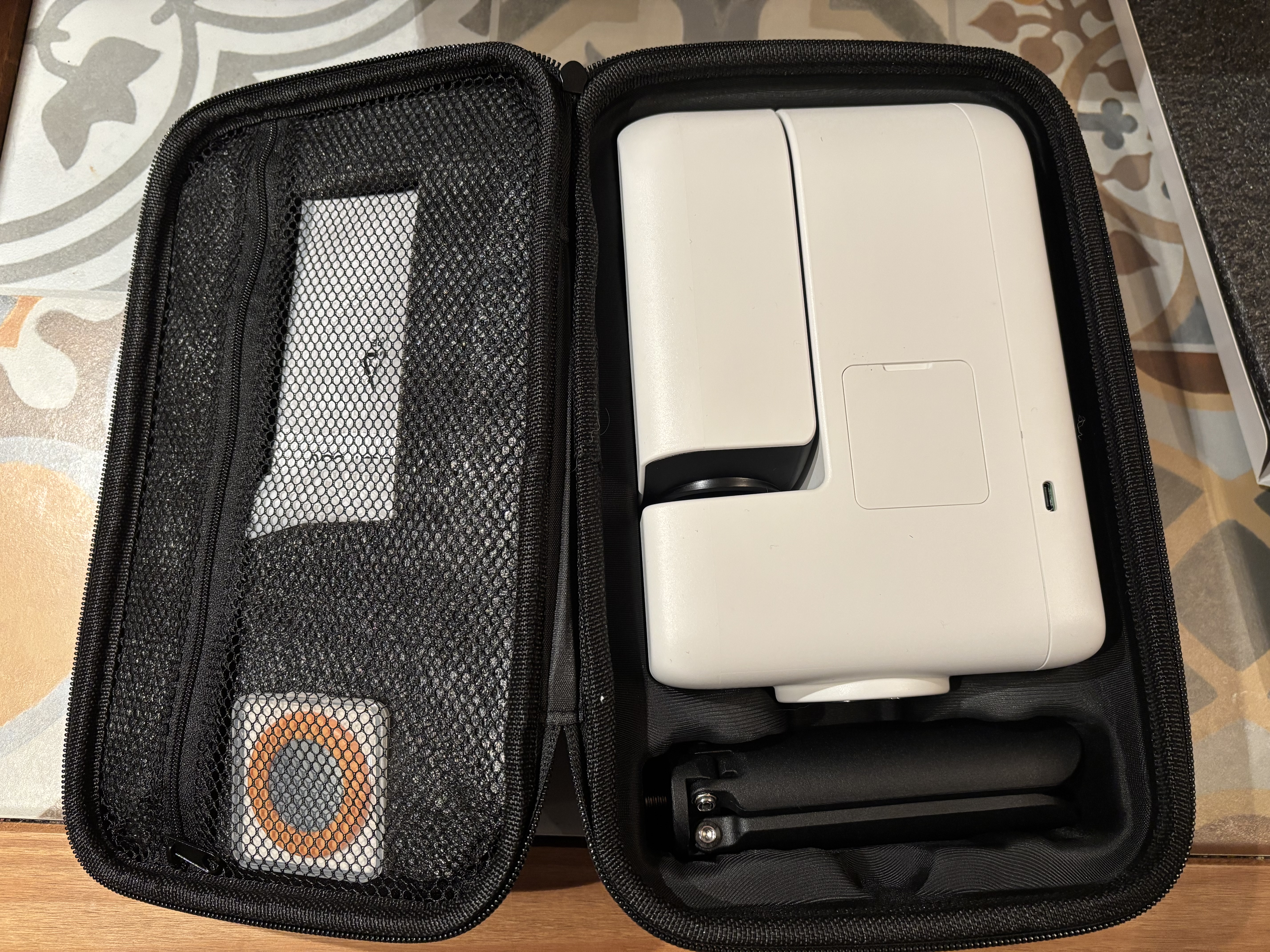 A carry bag is opened up and inside is a black tripod (folded) , a white smart telescope (also folded) on the left while on the right, some accessories are in a zipped-up section.