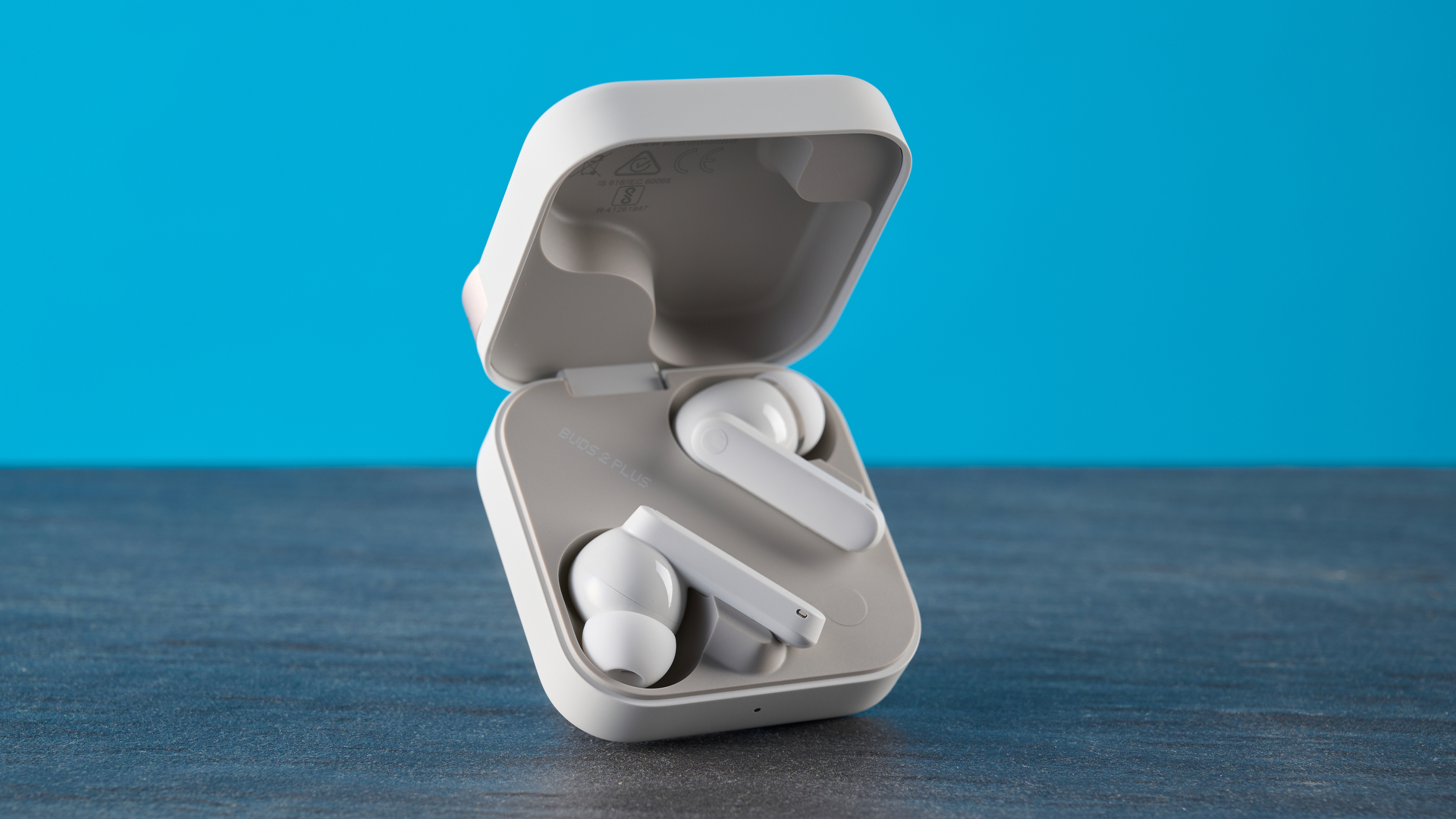 CMF Buds 2 Plus in light gray photographed in front of a blue background