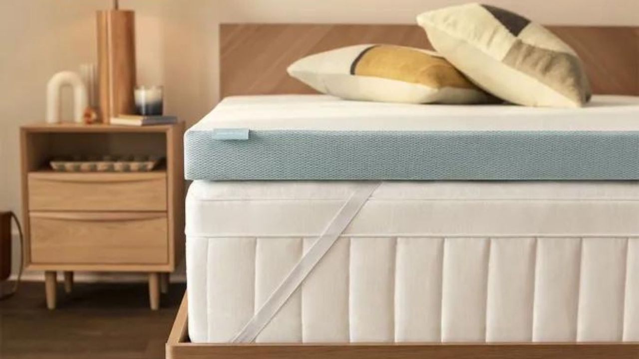 Corner of a Tempur-Pedic mattress topper on a bed beside a nightstand.