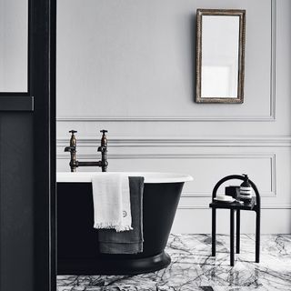 monochrome bathroom with marble stone flooring and black freestanding bath tub