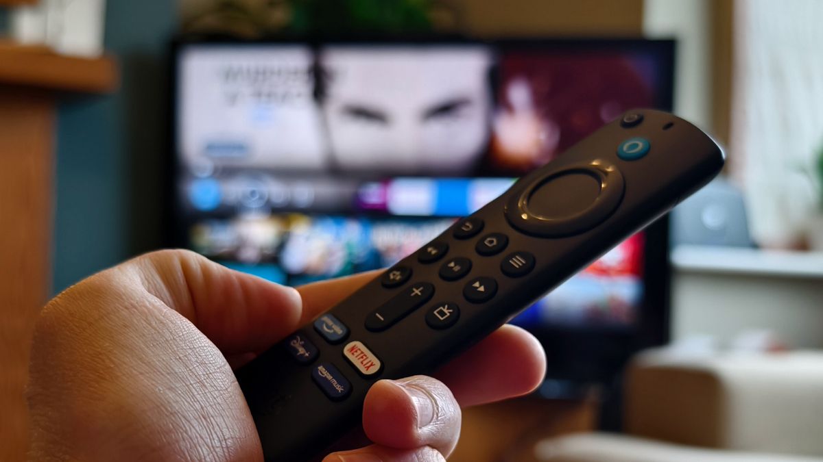 The Amazon Fire TV Stick being held in front of a TV displaying Fire TV.