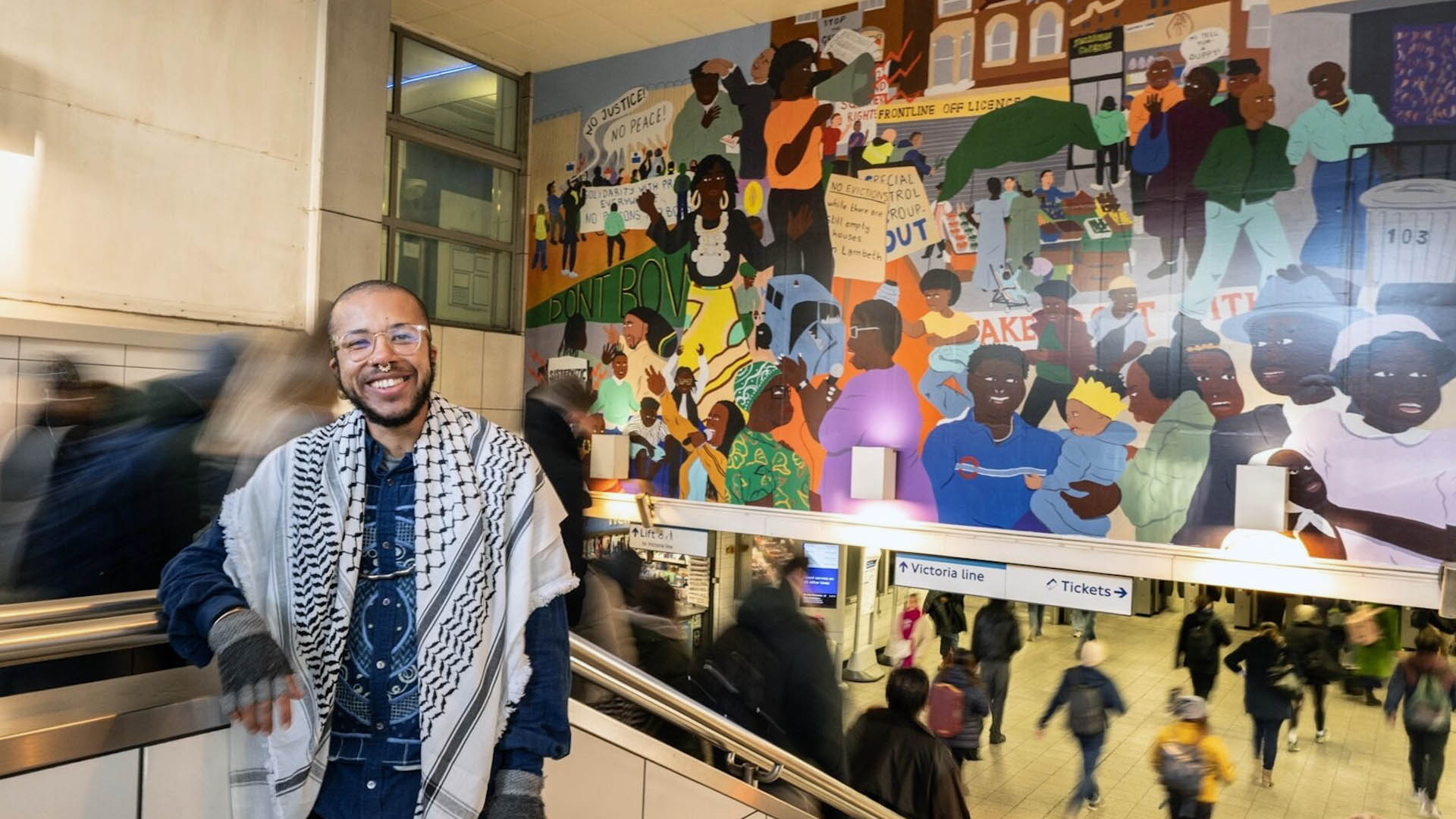 A photograph of artist Rudy Loewe in front of their mural. 