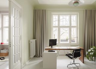 A home office with sage green walls and beige curtains