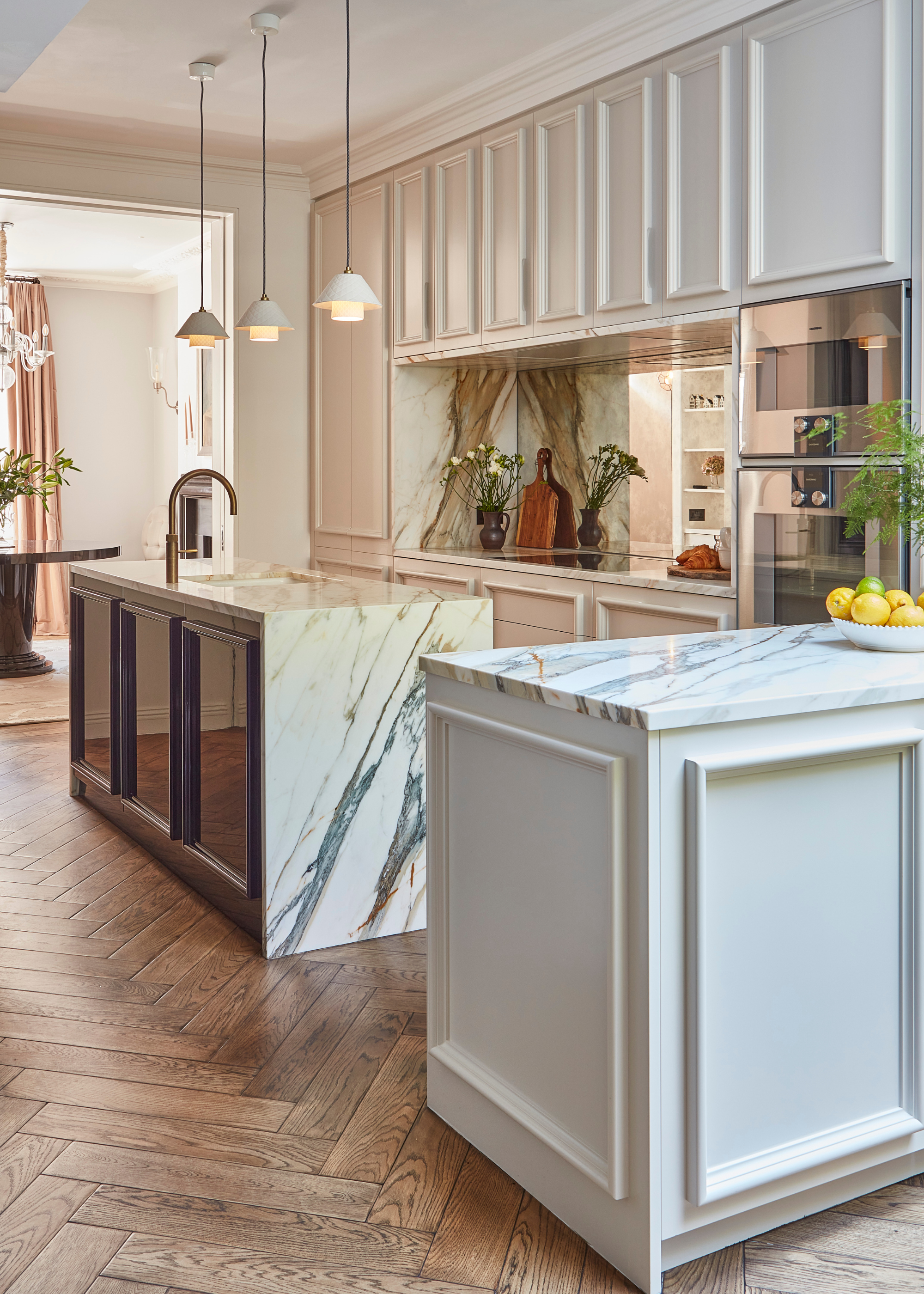 A modern kitchen with light kitchen cabinets, striking marble countertops and island with a dark gloss cabinet detail on one side with three pendant lights hanging above the island