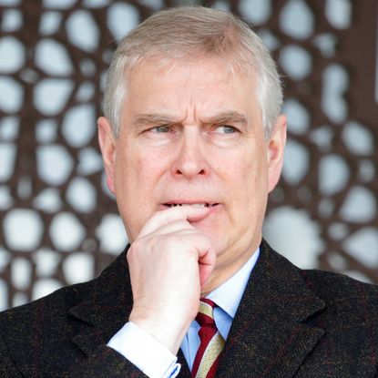 Prince Andrew wearing a suit putting his finger to his mouth