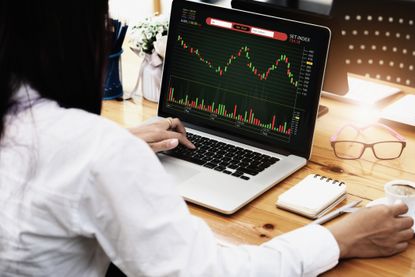 woman looking at a stock chart on her laptop while drinking coffee