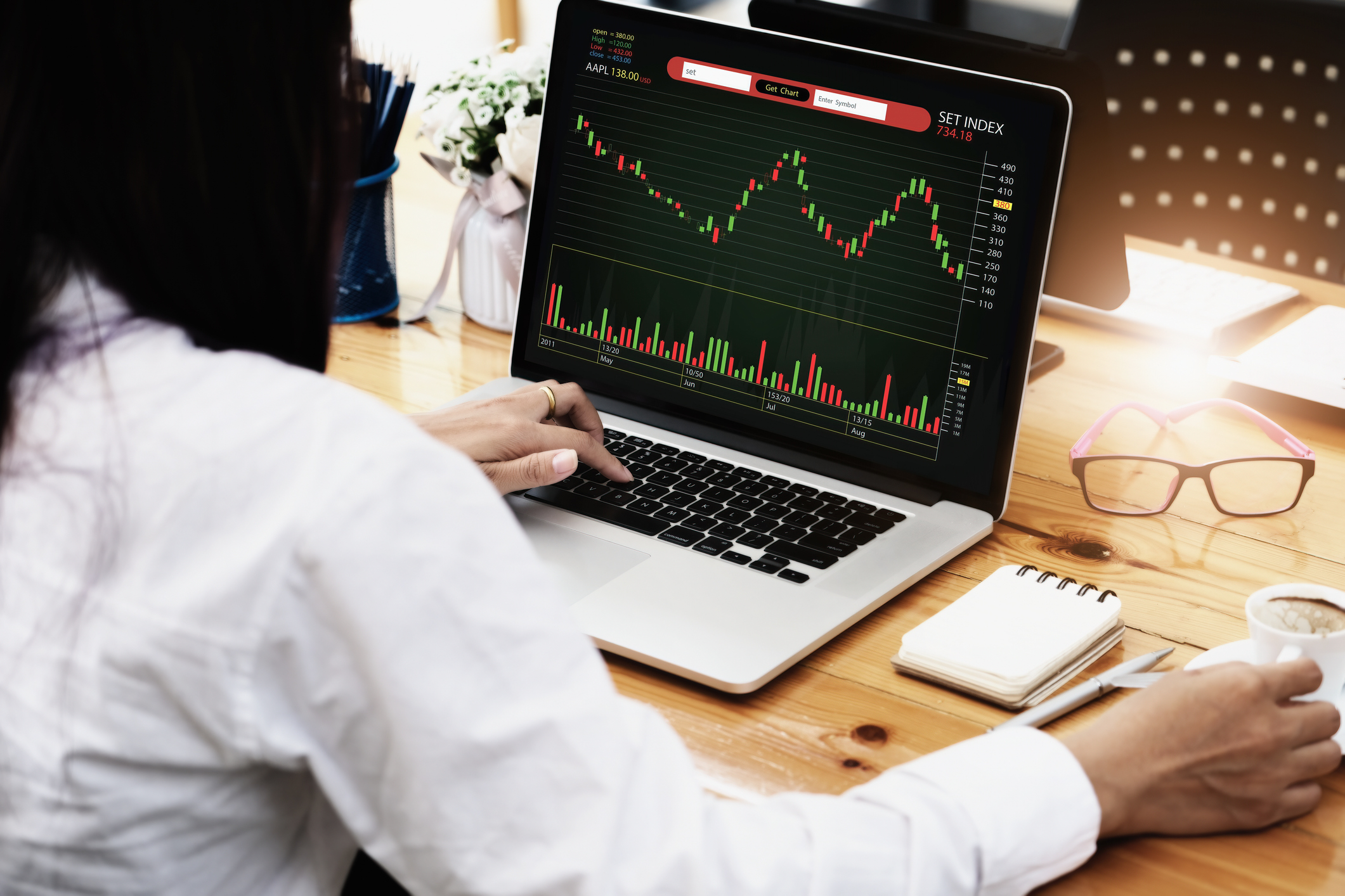 woman looking at a stock chart on her laptop while drinking coffee