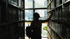 Female college student in silhouette standing in a college library and looking at books