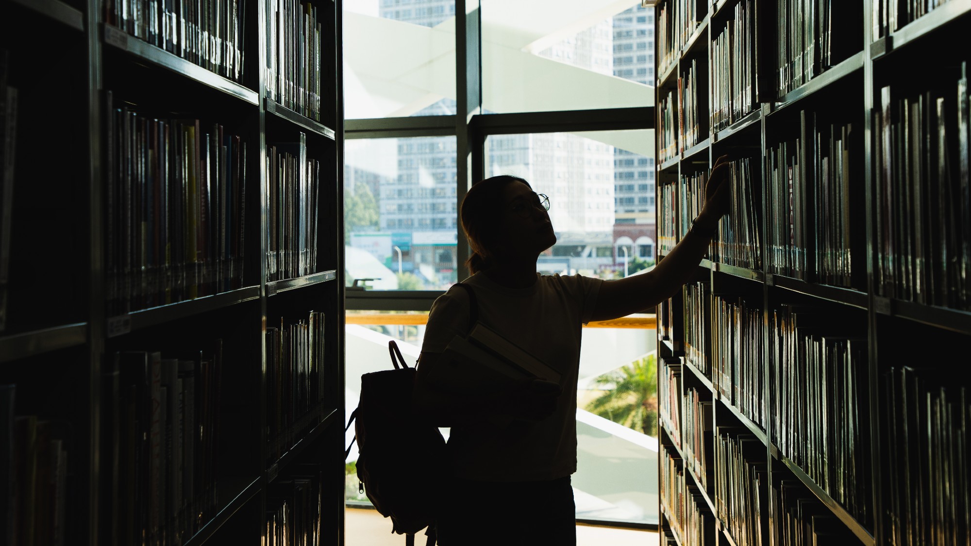 Female college student in silhouette standing in a college library and looking at books