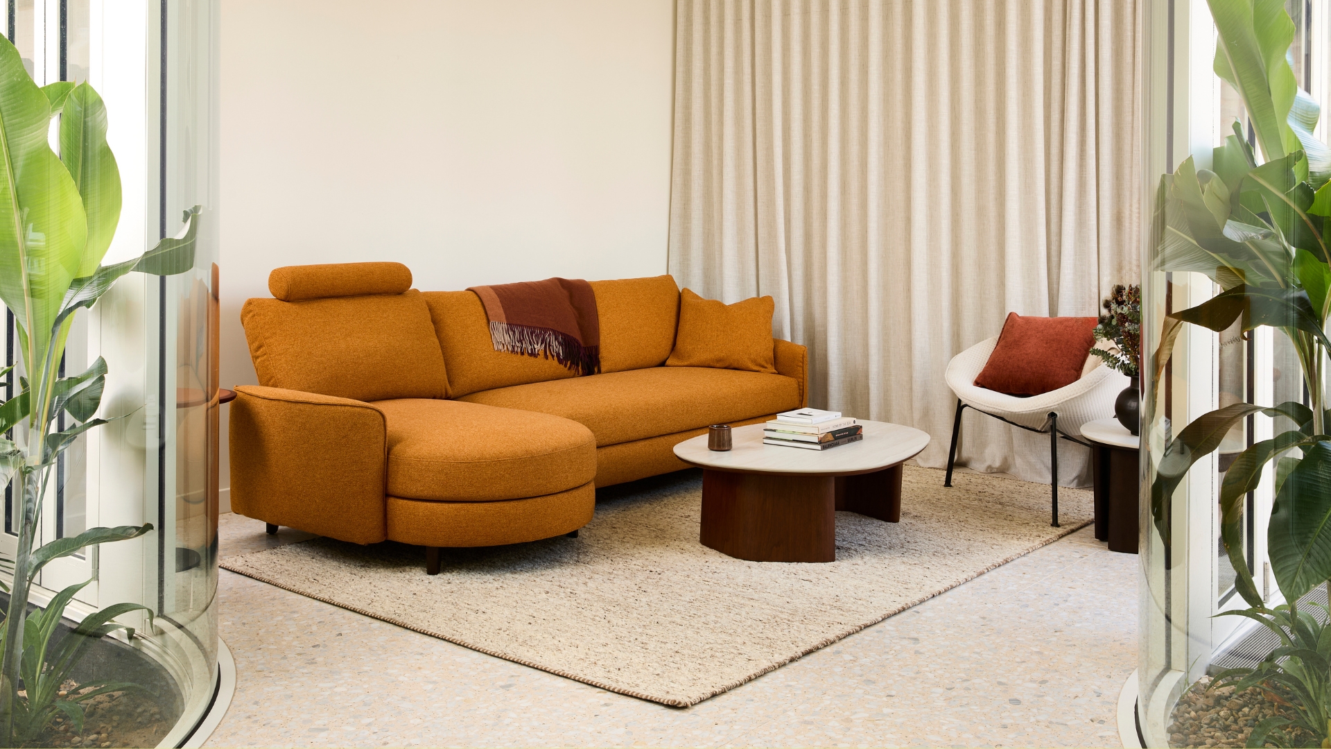 A burnt mustard modular stacked style sofa from King Living in a living room with glass walled gardens in view