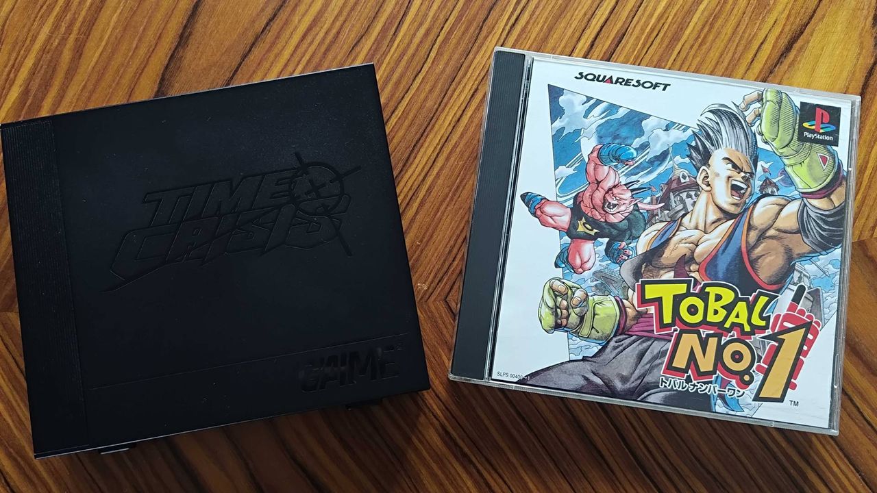 G'AIM'E Time Crisis console next to PS1 Tobal No 1 box on woodgrain table.