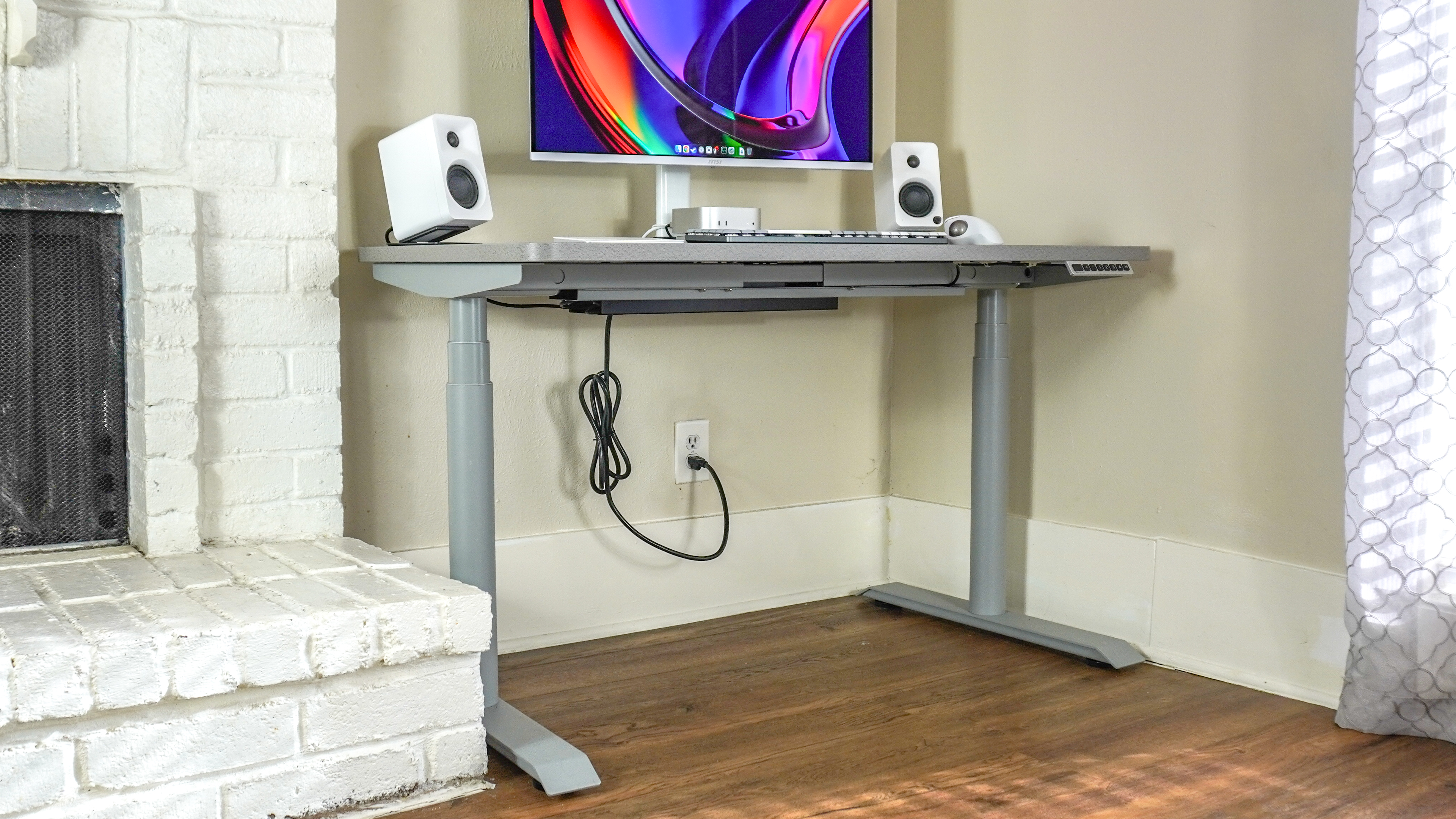 The Hinomi S1 standing desk set up in a corner next to a fireplace
