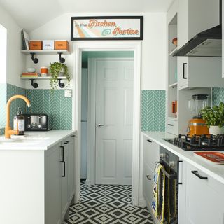 Kitchen with grey cupboards and white tops with under counter oven and hop and green backsplash tiles