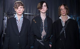 3 male models in netted clothing & dark suit jackets
