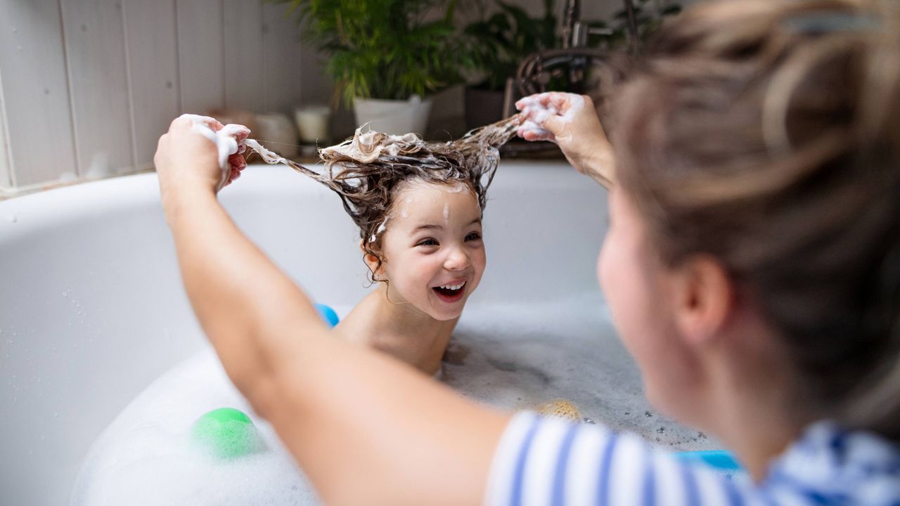 A mother gives her smiling daughter a bath.