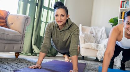 Two women in the high plank position in a living room
