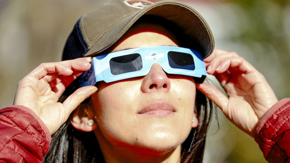 A young woman wears blue solar eclipse glasses to observe a wonder of nature