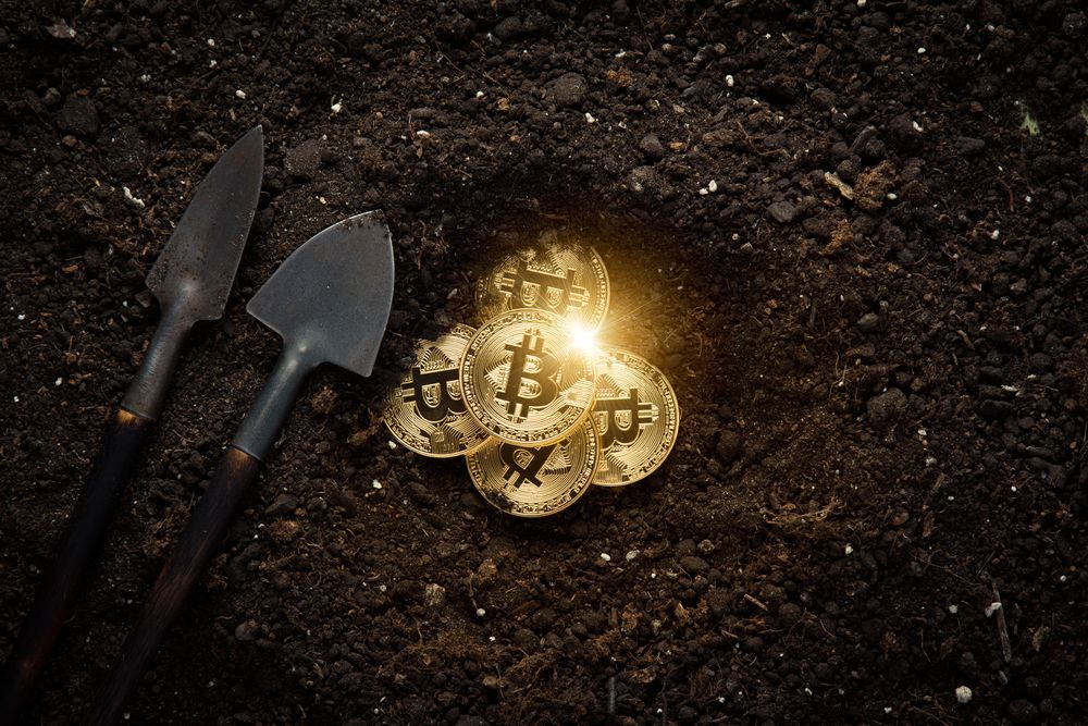 Two shovels next to Bitcoins being uncovered in mud to depict cryptocurrency mining