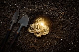 Two shovels next to Bitcoins being uncovered in mud to depict cryptocurrency mining