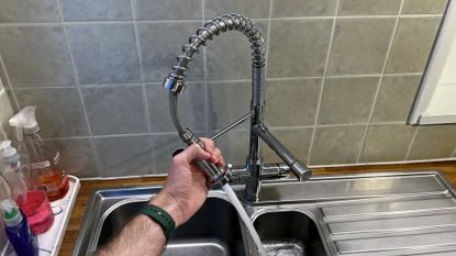 Fohen Flex tap in a kitchen, being held by a hand while water sprays