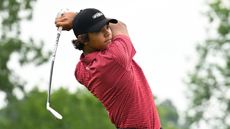 Charlie Woods wearing a red polo and black cap hits an iron shot