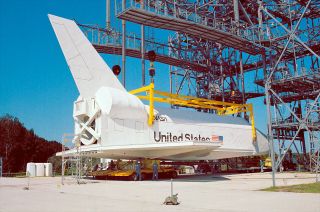 a full-size white space shuttle simulator sits beneath a set of scaffolding under a blue sky