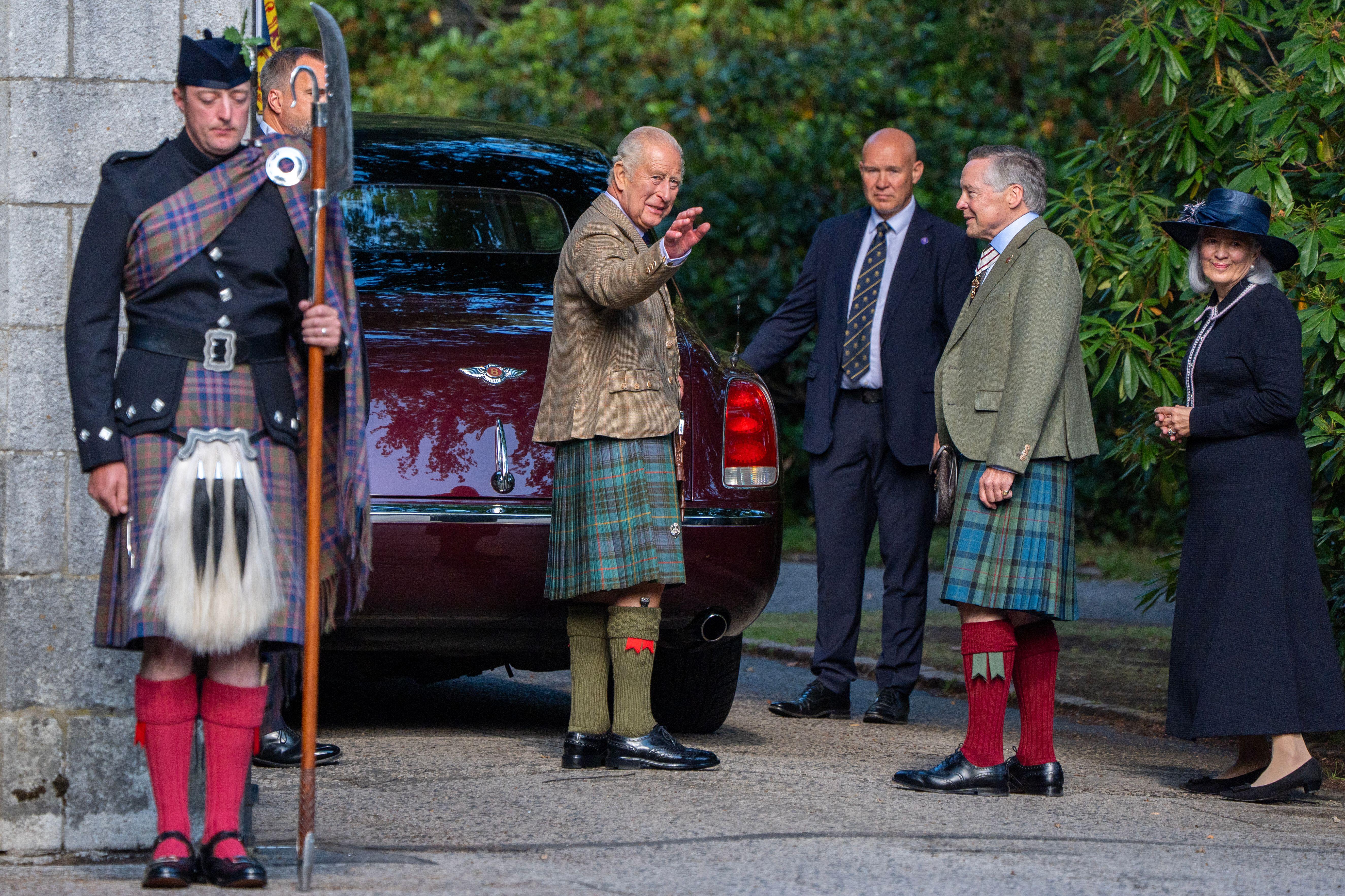 King Charles in a kilt waving in front of a car