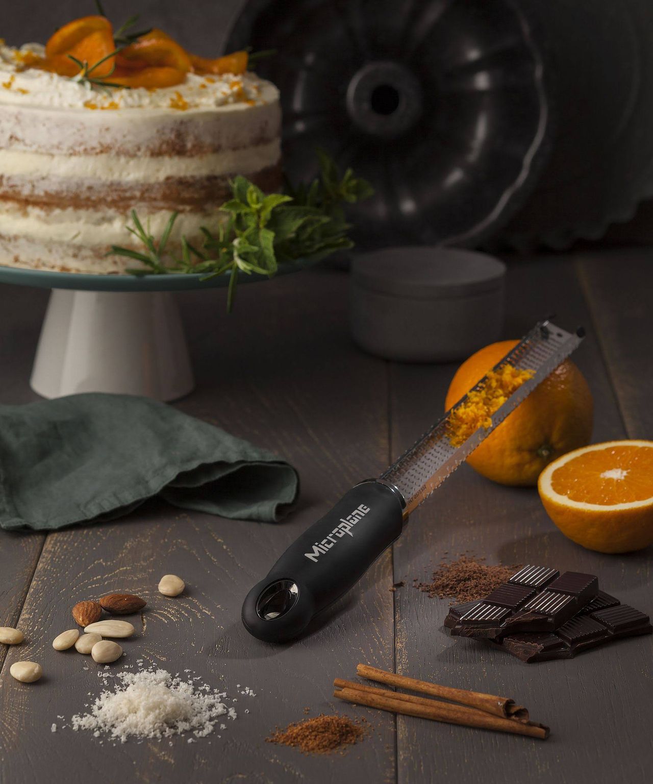 A Microplane premium zester grater used to shave orange peel from fruit with cake in background