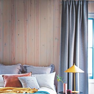 A bedroom with wood wall panelling and a blue long curtain covering a window next to the bed